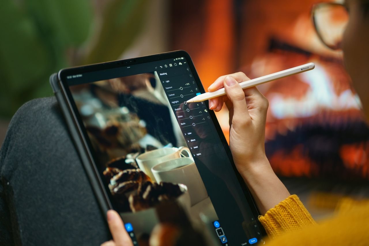 A person editing photos on a tablet with a stylus by a cozy fireplace setting.
