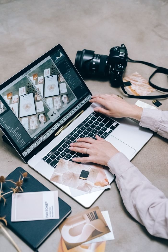 Hands editing photos on a laptop with a camera nearby, showcasing modern technology and creativity.